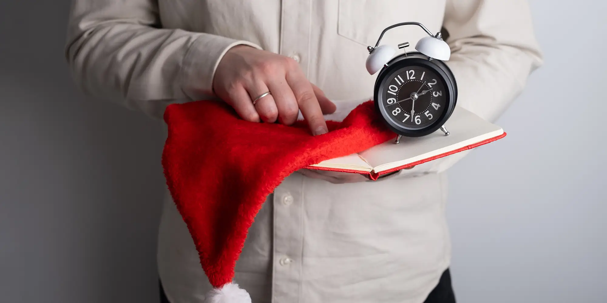 person holding a journal, clock, and Santa hat in preparation for holiday marketing